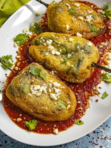 A platter of Chiles Rellenos served on a plate over salsa roja